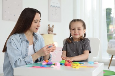 Smiling mother and her daughter sculpting with play dough at table indoors