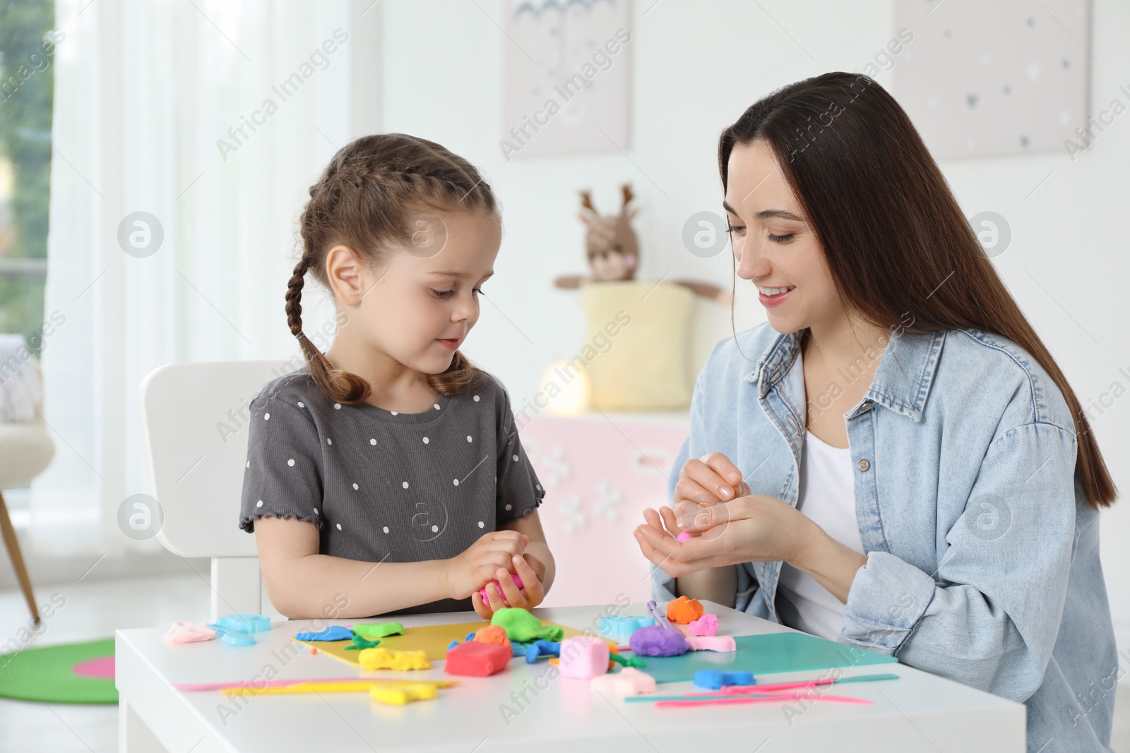 Photo of Smiling mother and her daughter sculpting with play dough at table indoors