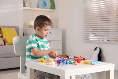 Photo of Little boy sculpting with play dough at table indoors