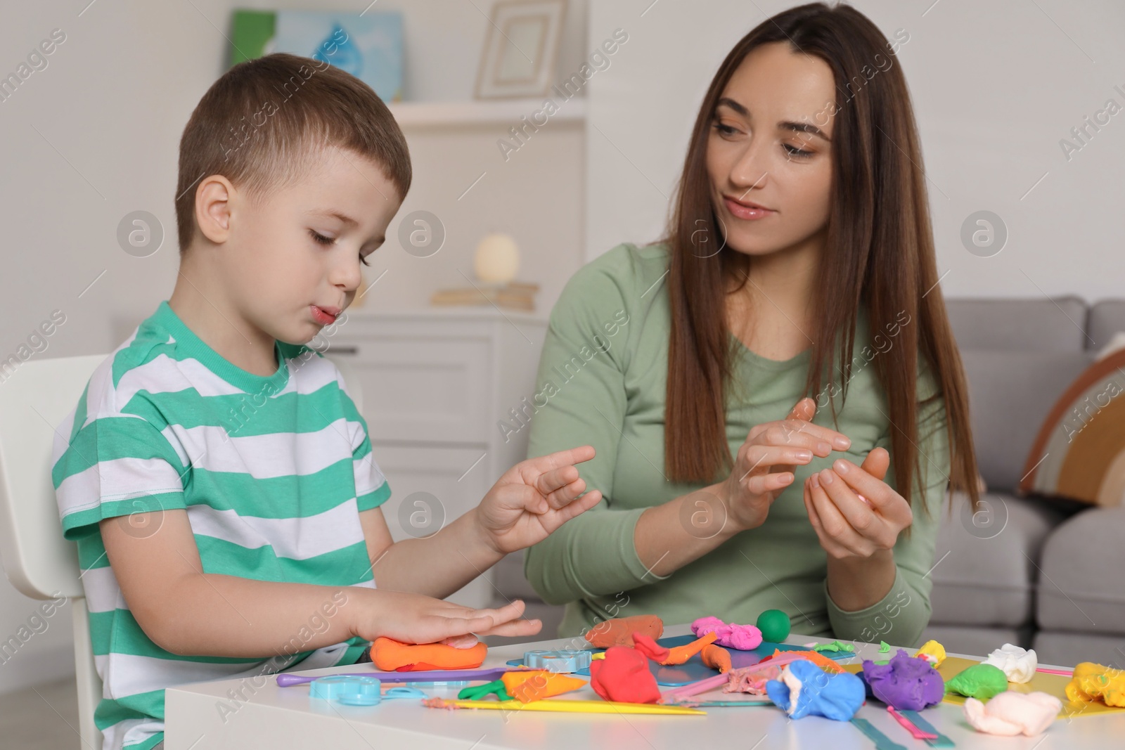 Photo of Son and mother sculpting with play dough at table indoors