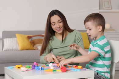 Photo of Smiling mother and her son sculpting with play dough at table indoors