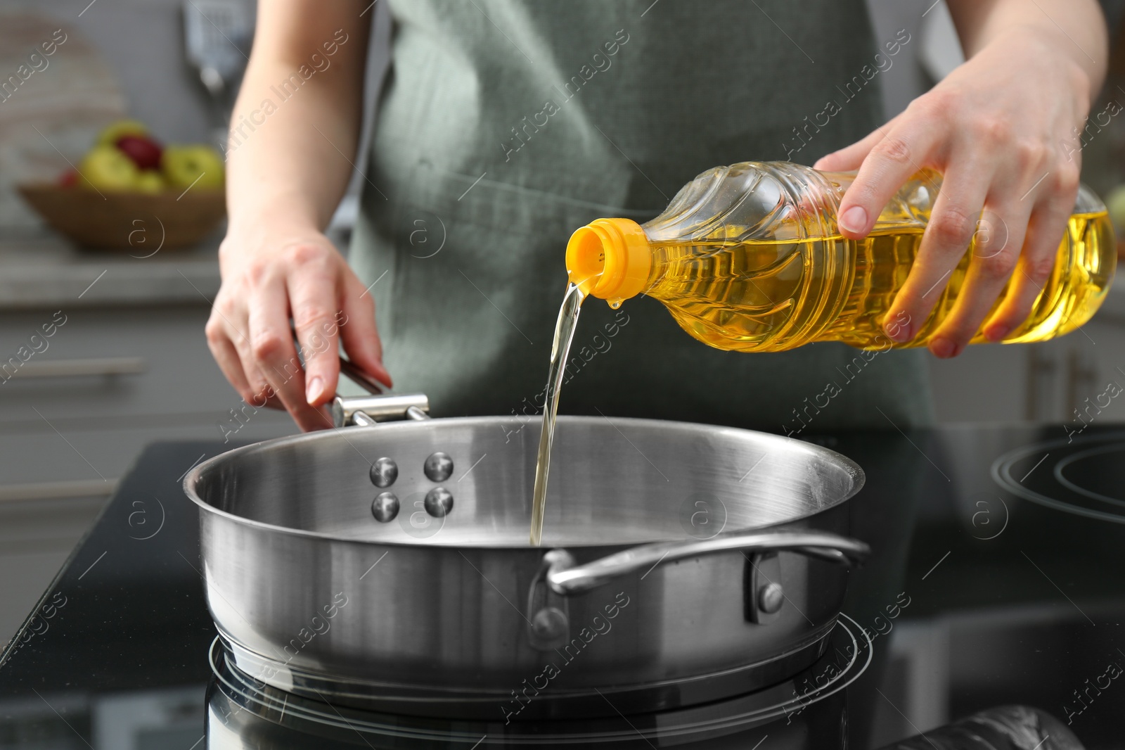 Photo of Vegetable fats. Woman pouring oil into frying pan on stove in kitchen, closeup