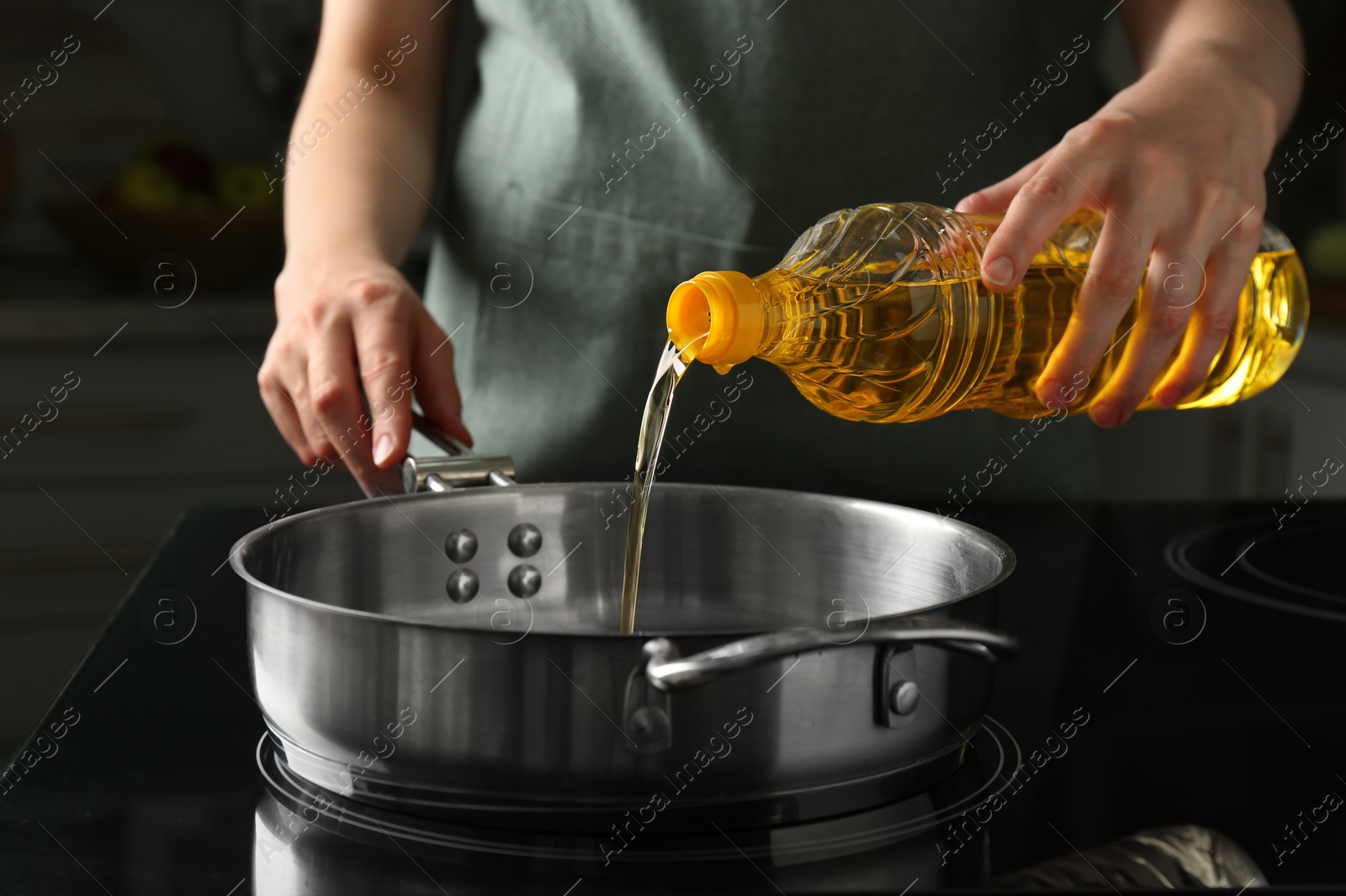 Photo of Vegetable fats. Woman pouring oil into frying pan on stove in kitchen, closeup