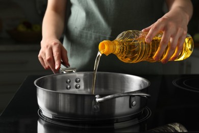 Vegetable fats. Woman pouring oil into frying pan on stove in kitchen, closeup