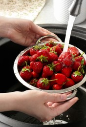 Photo of Woman washing fresh strawberries under tap water in metal colander above sink, closeup