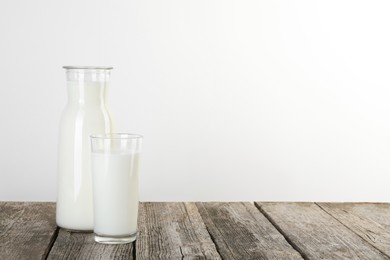 Carafe and glass of fresh milk on wooden table, space for text