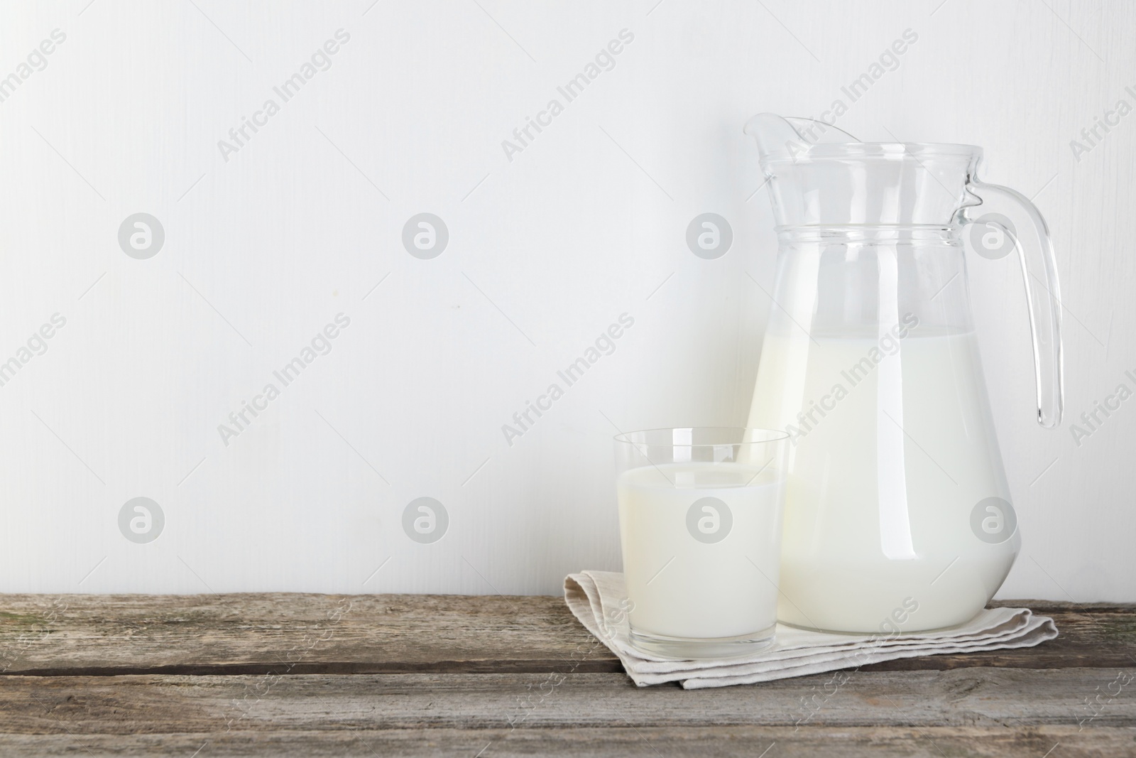 Photo of Jug and glass of fresh milk on wooden table, space for text