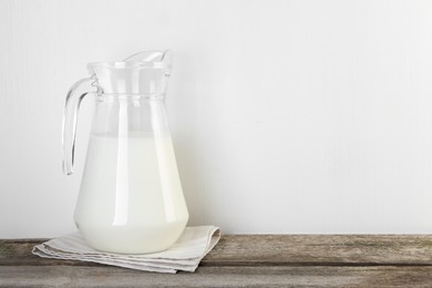 Jug of fresh milk on wooden table, space for text
