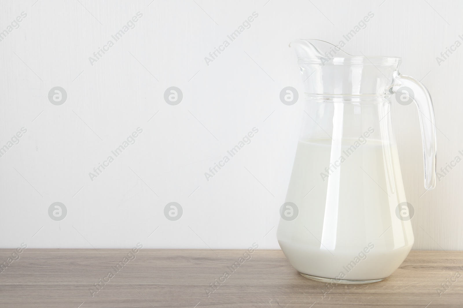 Photo of Jug of fresh milk on wooden table, space for text