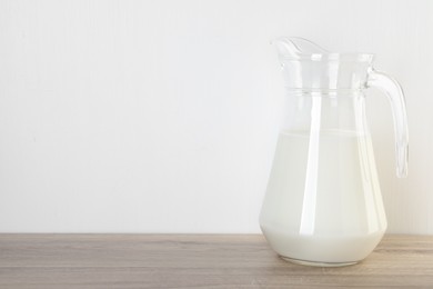 Jug of fresh milk on wooden table, space for text