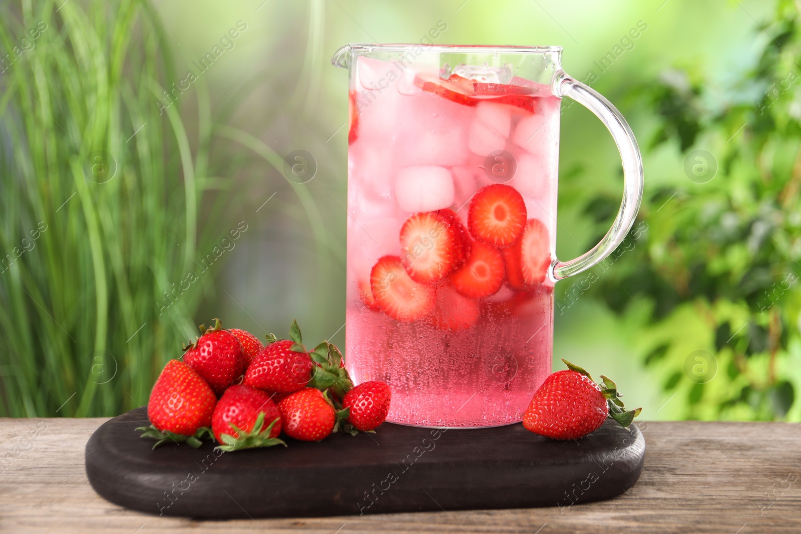 Photo of Freshly made strawberry lemonade in jug on wooden table outdoors