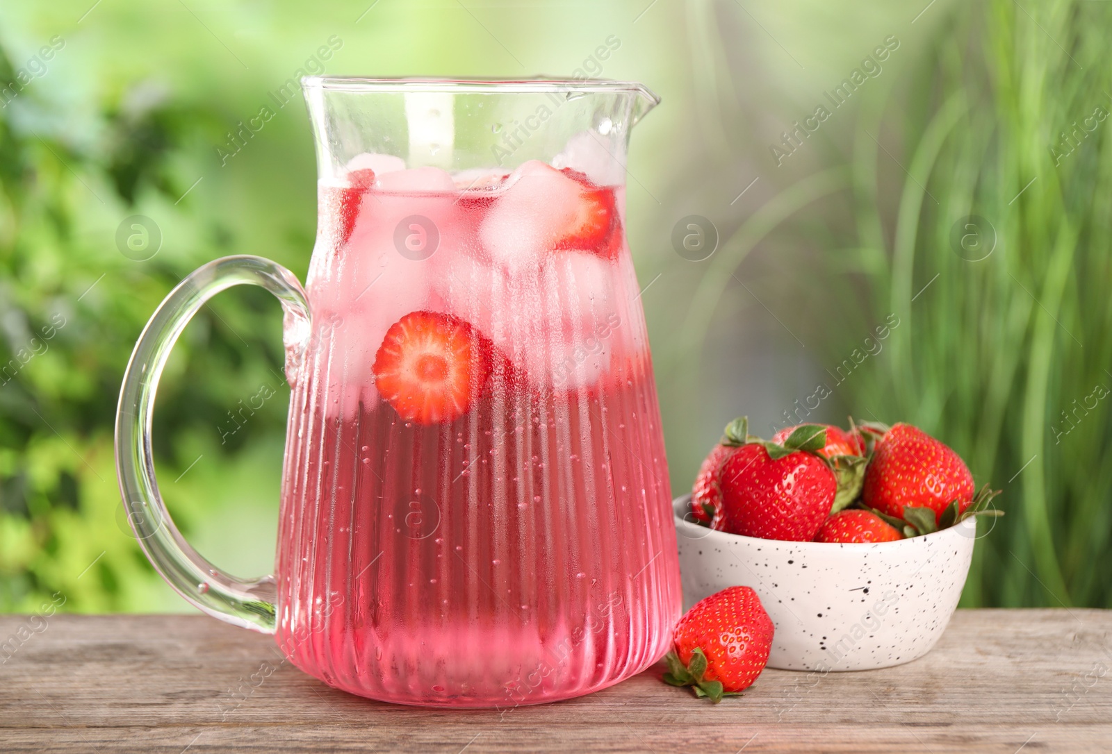 Photo of Freshly made strawberry lemonade in jug on wooden table outdoors