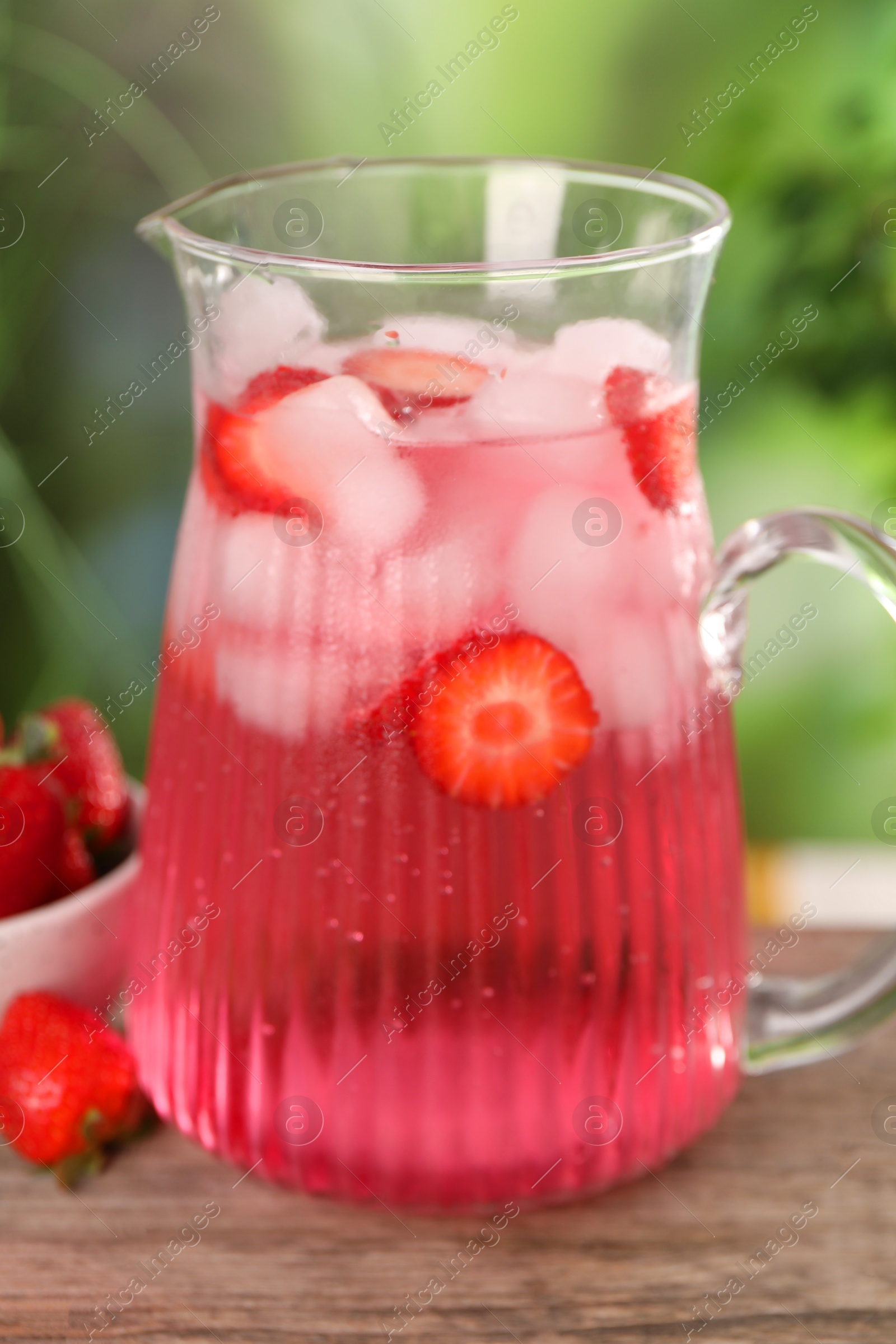 Photo of Freshly made strawberry lemonade in jug on wooden table outdoors