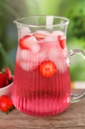 Photo of Freshly made strawberry lemonade in jug on wooden table outdoors