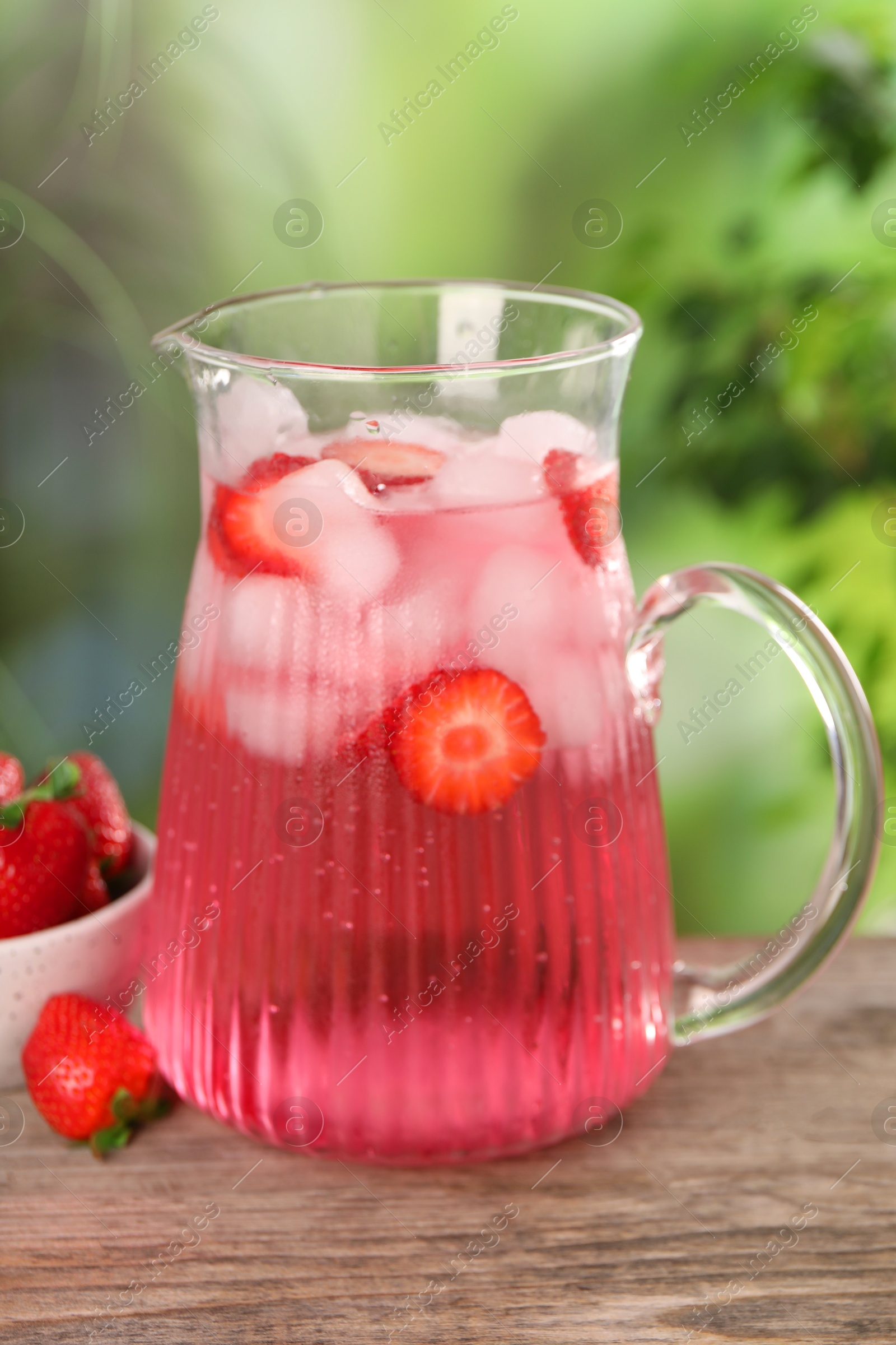 Photo of Freshly made strawberry lemonade in jug on wooden table outdoors