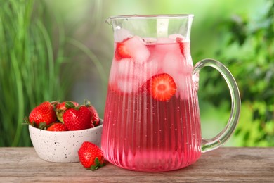 Photo of Freshly made strawberry lemonade in jug on wooden table outdoors