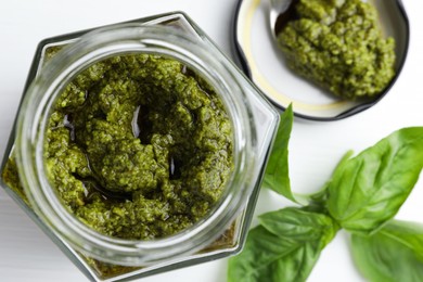 Tasty pesto sauce in jar and basil on white table, top view