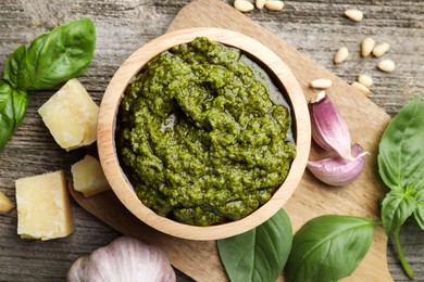 Photo of Tasty pesto sauce, basil, pine nuts, cheese and garlic on wooden table, top view