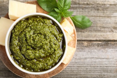 Tasty pesto sauce in bowl, basil and cheese on wooden table, top view. Space for text