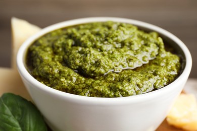 Photo of Tasty pesto sauce in bowl and basil on table, closeup