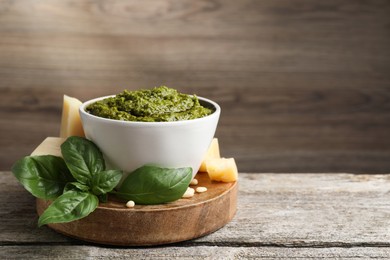 Photo of Tasty pesto sauce in bowl, basil, cheese and pine nuts on wooden table, space for text