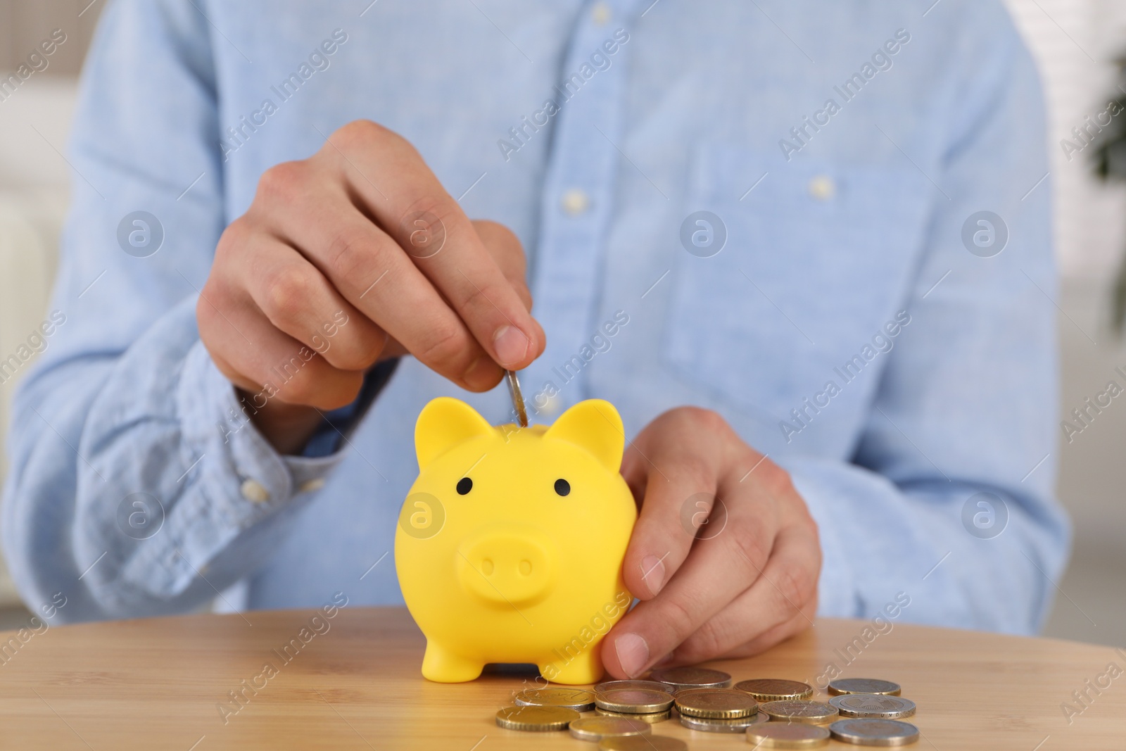 Photo of Man putting coin into yellow piggy bank on wooden table, closeup