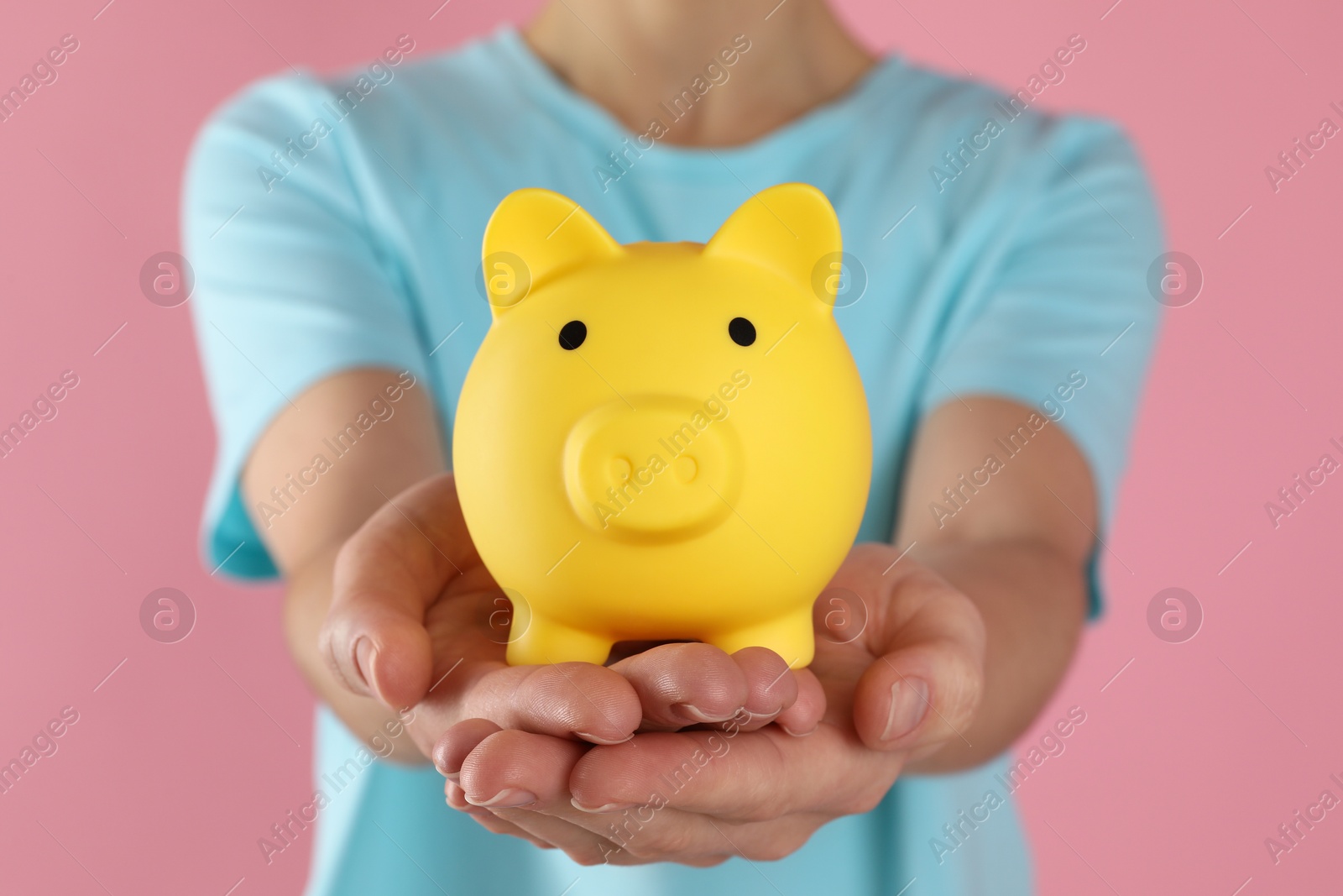 Photo of Woman with yellow piggy bank on pink background, closeup