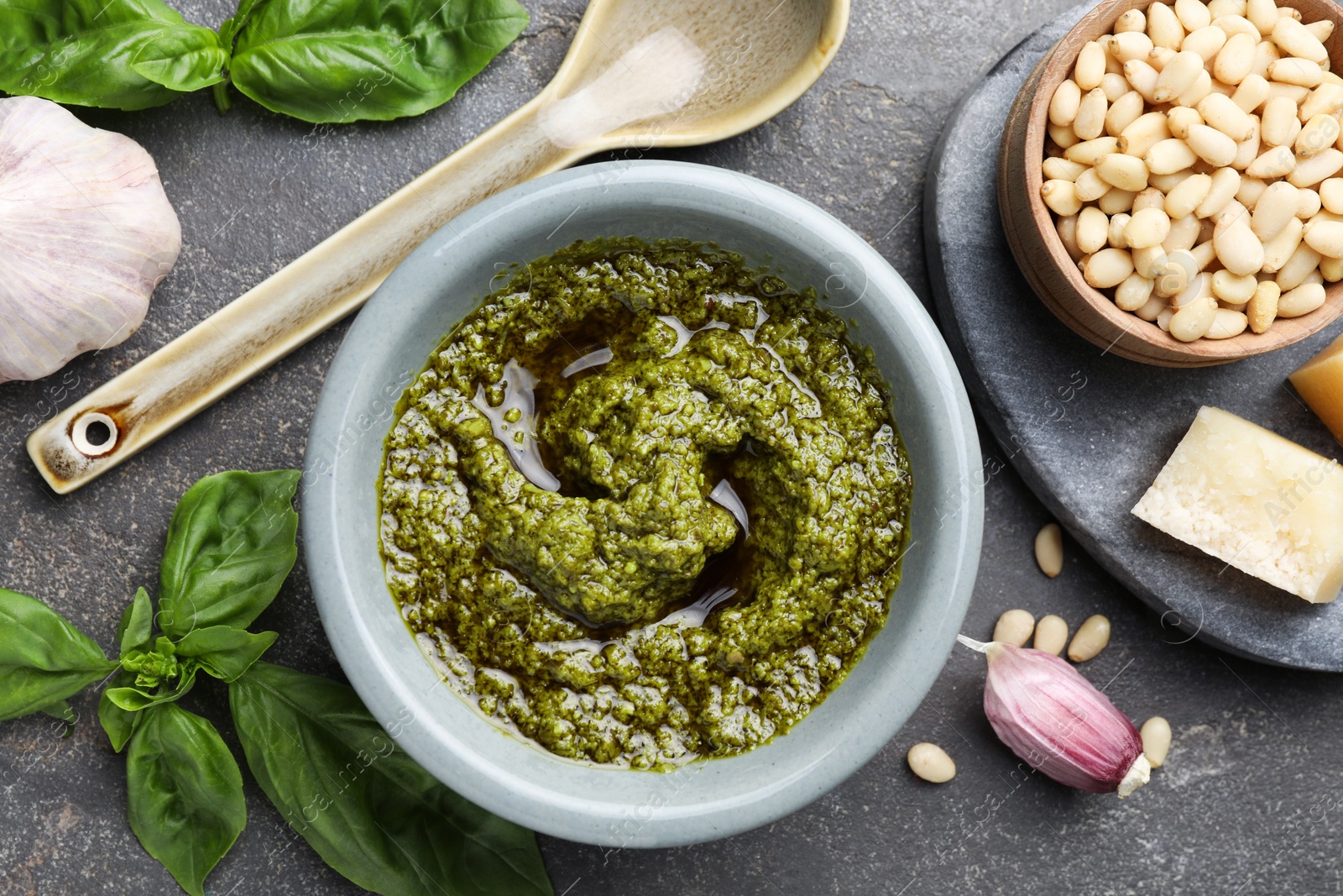 Photo of Tasty pesto sauce in bowl, basil, pine nuts, cheese and garlic on grey table, flat lay