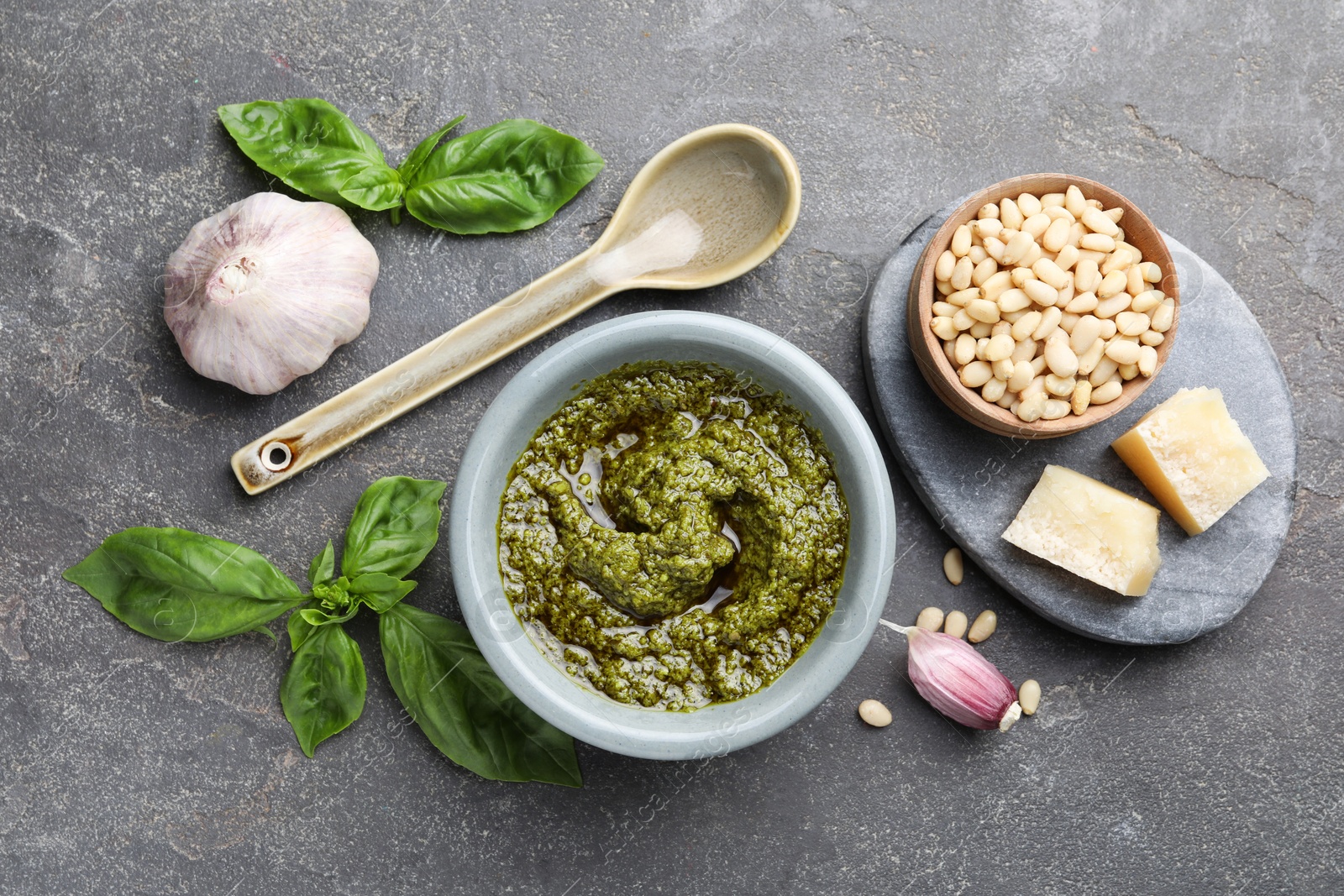 Photo of Tasty pesto sauce in bowl, basil, pine nuts, cheese and garlic on grey table, flat lay