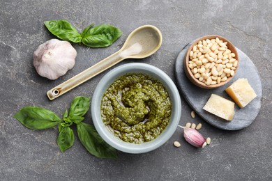 Tasty pesto sauce in bowl, basil, pine nuts, cheese and garlic on grey table, flat lay