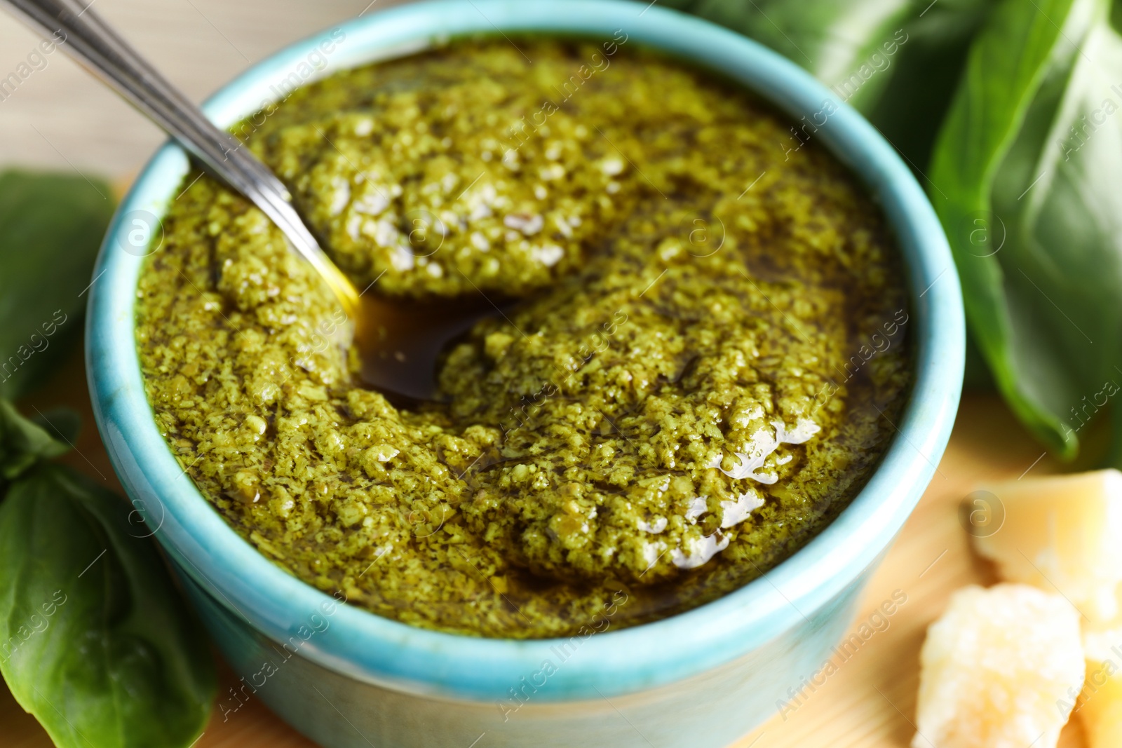 Photo of Tasty pesto sauce in bowl, spoon, cheese and basil on table, closeup