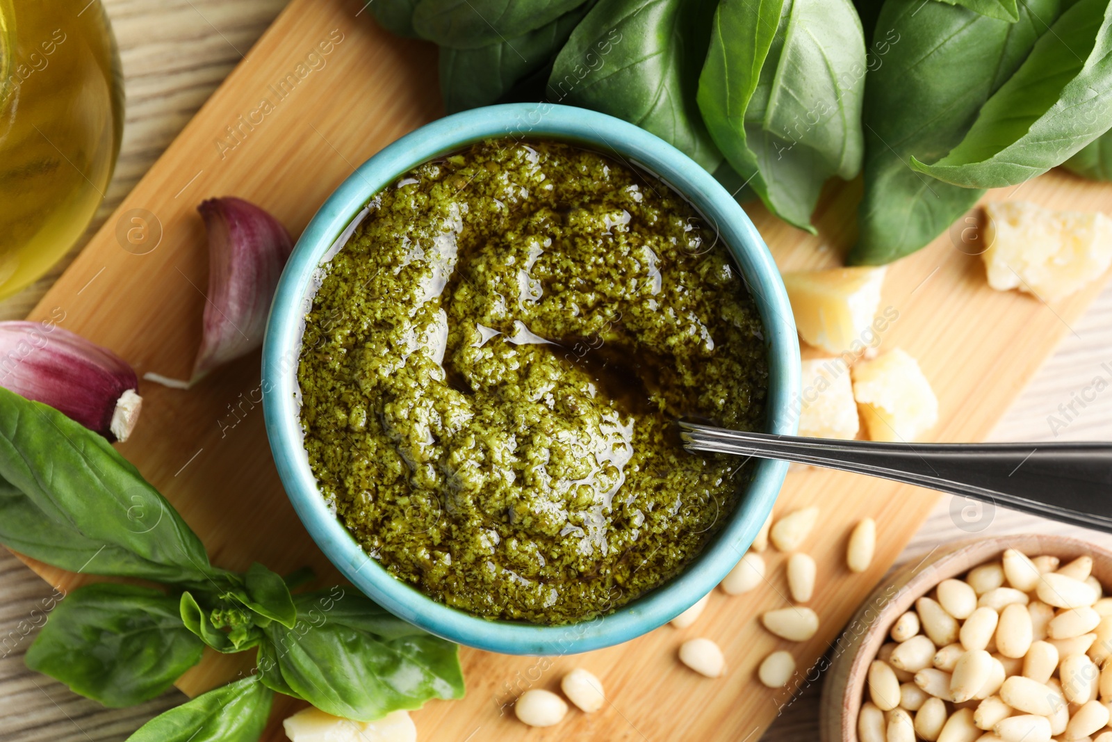 Photo of Tasty pesto sauce in bowl, basil, pine nuts, cheese and garlic on wooden table, top view