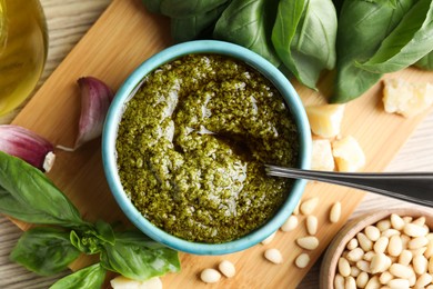 Tasty pesto sauce in bowl, basil, pine nuts, cheese and garlic on wooden table, top view