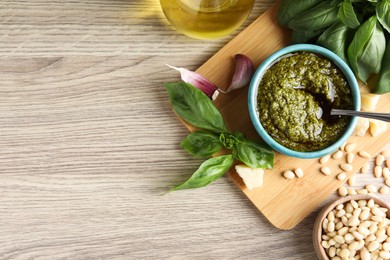 Photo of Tasty pesto sauce in bowl, basil, pine nuts, cheese and garlic on wooden table, top view. Space for text