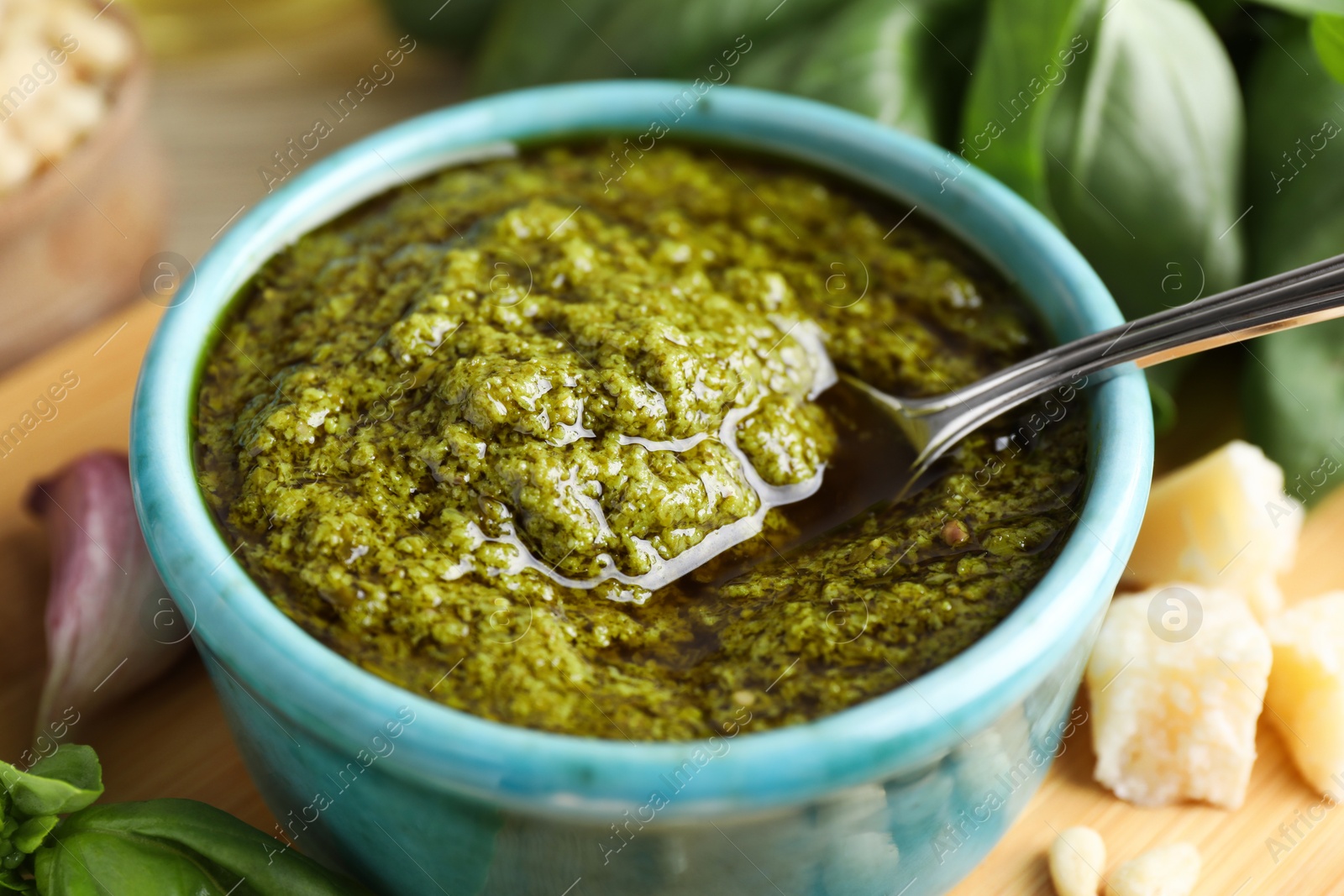 Photo of Tasty pesto sauce in bowl, spoon, cheese and basil on table, closeup