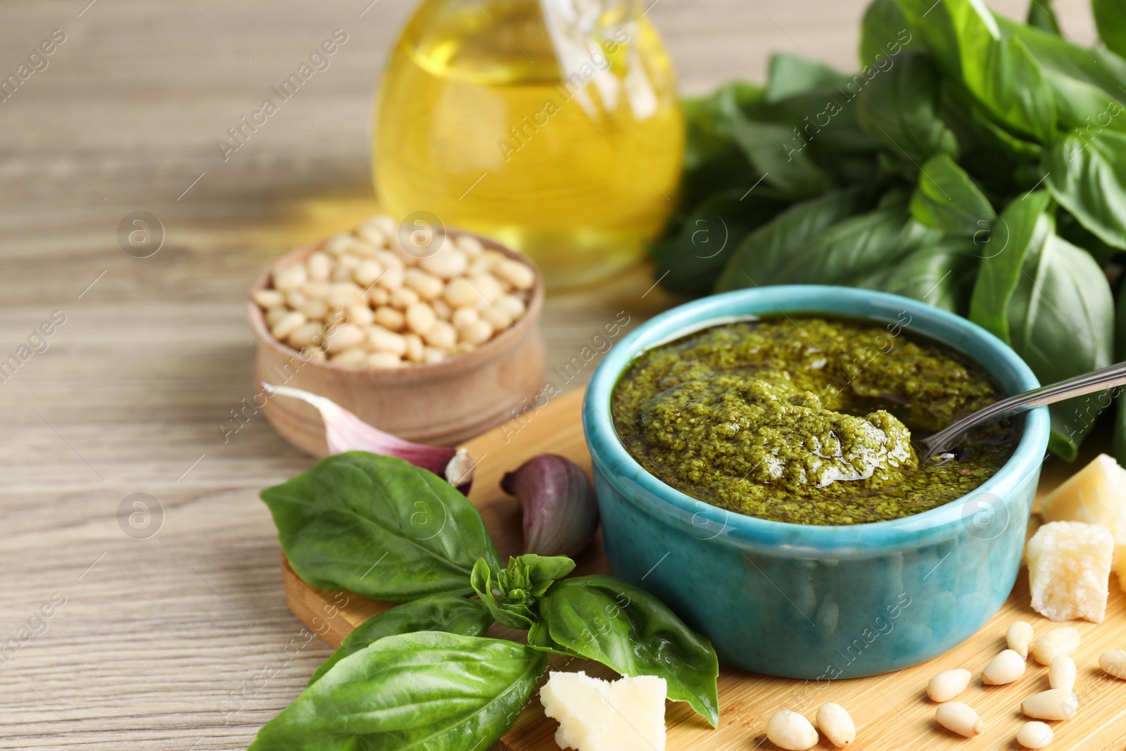 Photo of Tasty pesto sauce in bowl, basil, pine nuts, cheese and garlic on wooden table