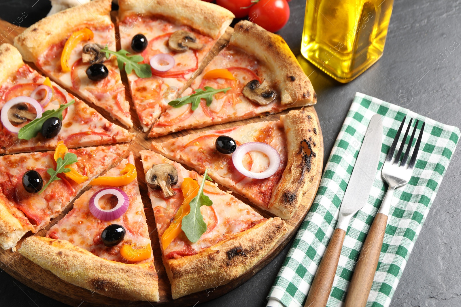 Photo of Cut delicious vegetarian pizza, cutlery and ingredients on black table, closeup