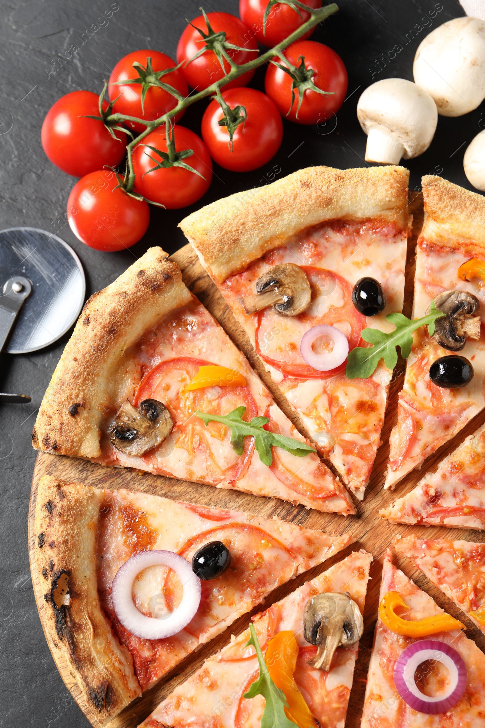 Photo of Cut delicious vegetarian pizza and ingredients on black table, flat lay