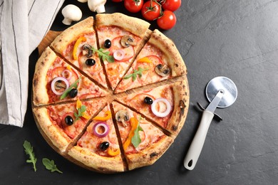 Photo of Cut delicious vegetarian pizza, cutter and ingredients on black table, flat lay