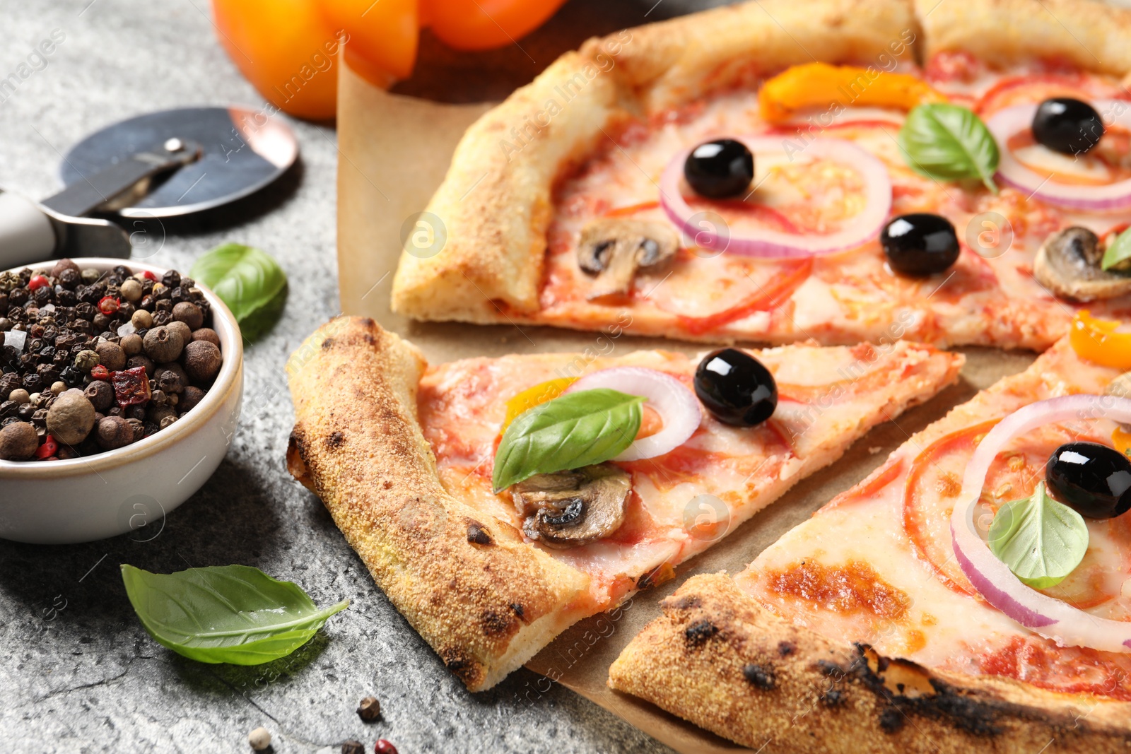 Photo of Cut delicious vegetarian pizza and peppercorns on grey table, closeup