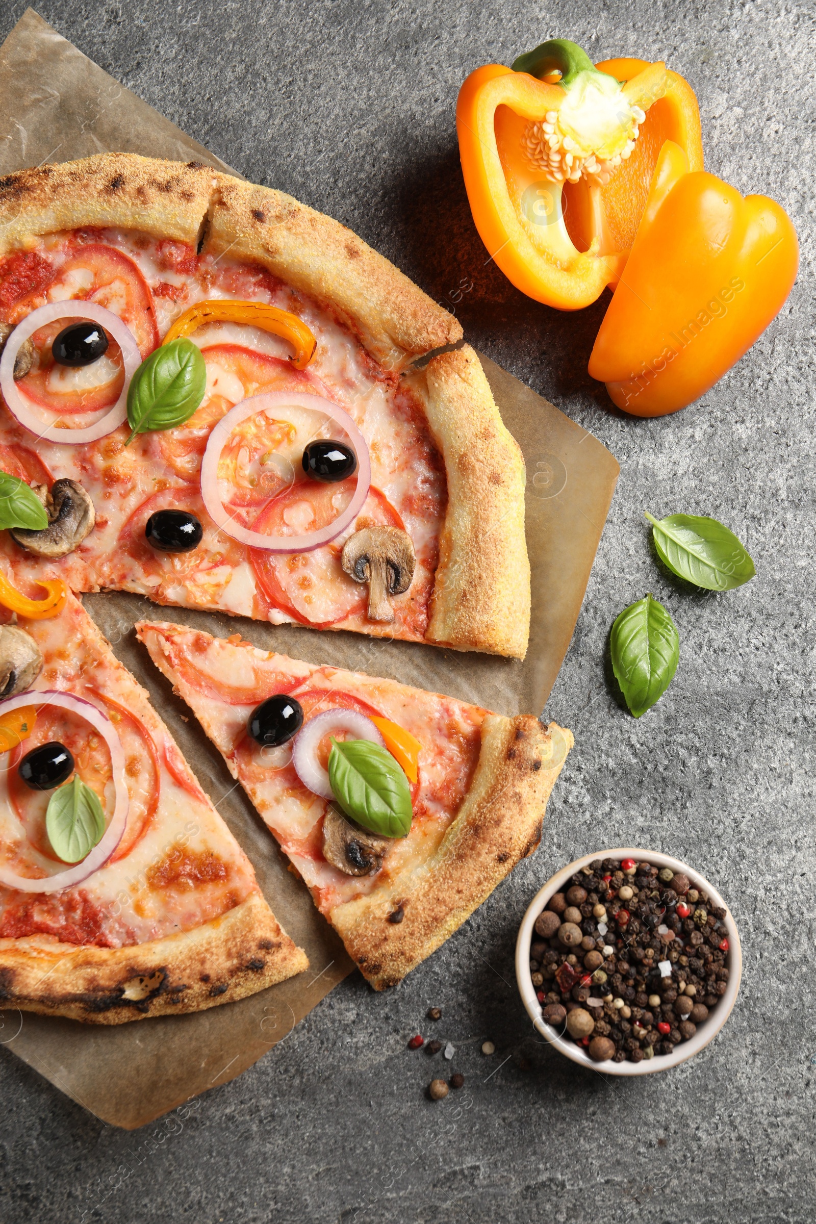 Photo of Cut delicious vegetarian pizza and ingredients on grey table, flat lay