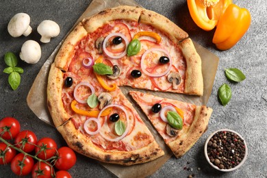 Photo of Cut delicious vegetarian pizza and ingredients on grey table, flat lay