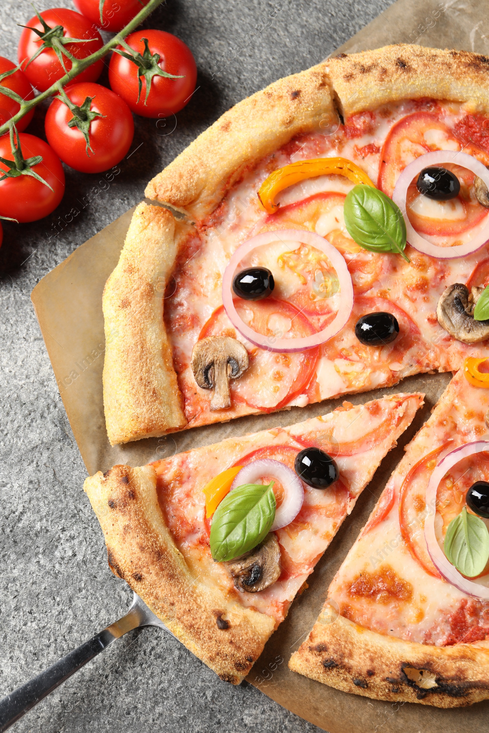 Photo of Cut delicious vegetarian pizza and tomatoes on grey table, closeup