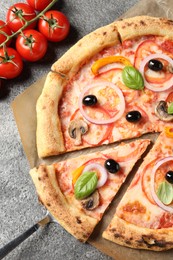 Photo of Cut delicious vegetarian pizza and tomatoes on grey table, closeup