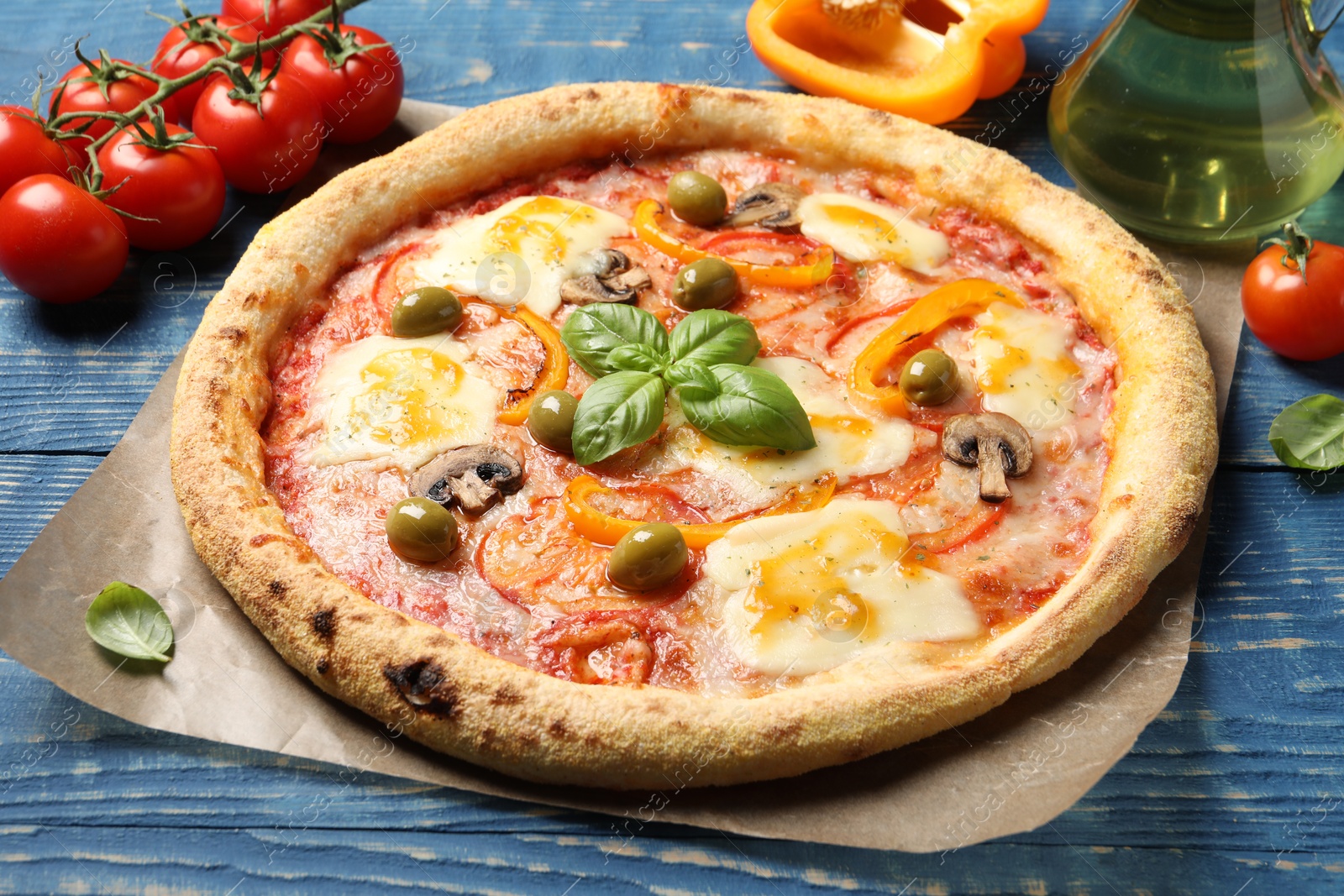 Photo of Delicious vegetarian pizza and ingredients on blue wooden table, closeup