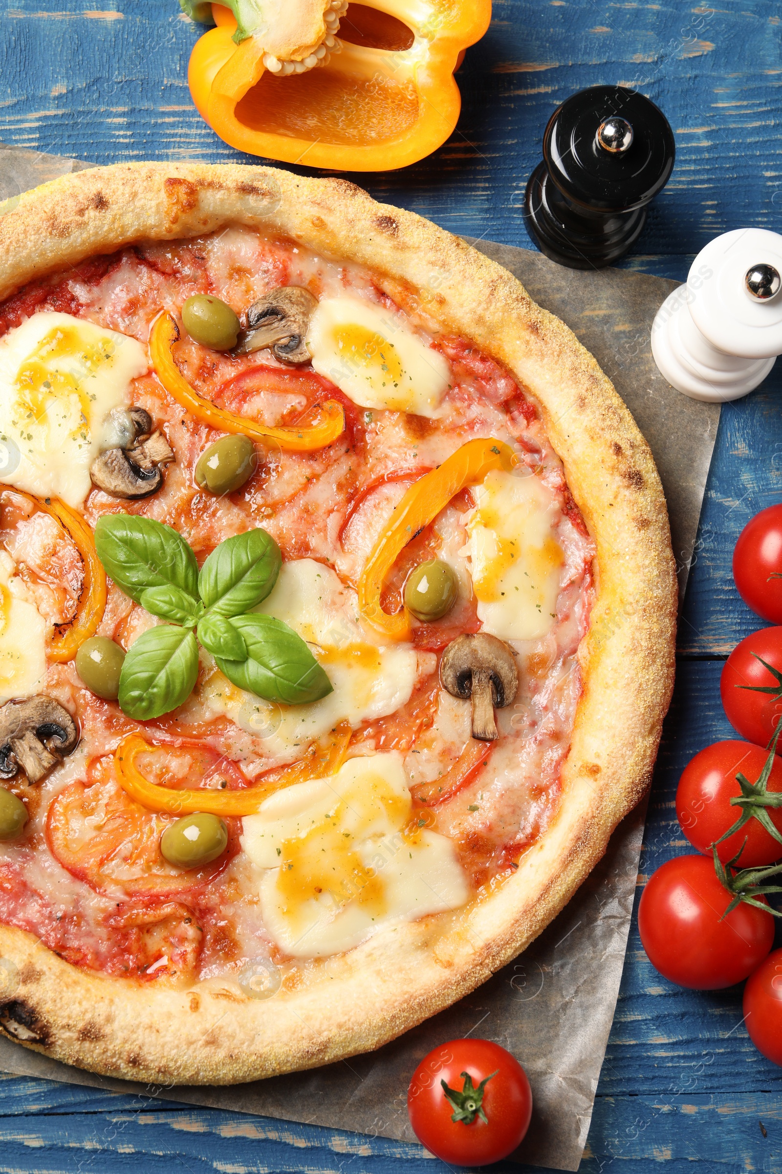 Photo of Delicious vegetarian pizza and ingredients on blue wooden table, top view