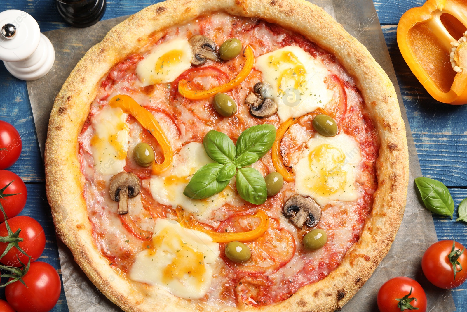 Photo of Delicious vegetarian pizza and ingredients on blue wooden table, top view