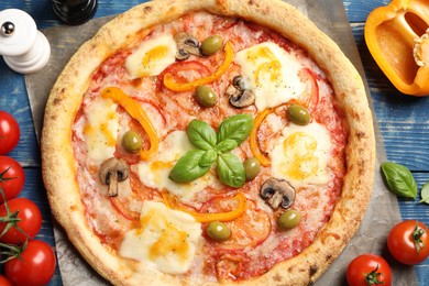 Photo of Delicious vegetarian pizza and ingredients on blue wooden table, top view