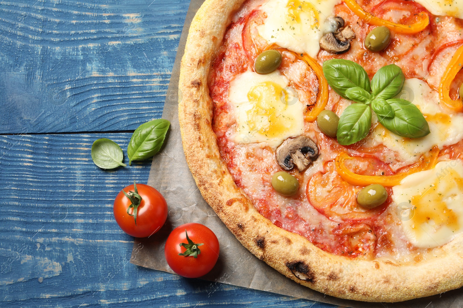 Photo of Delicious vegetarian pizza and ingredients on blue wooden table, top view