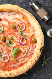 Photo of Delicious vegetarian pizza, arugula, salt and pepper on black table, top view